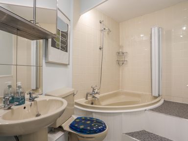 A bathroom with a corner bathtub shower toilet with a blue seat sink and mirrored cabinet at Alltwen in Borth-y-Gest