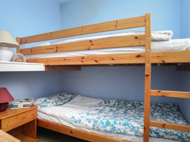 A bedroom with wooden bunk beds and a bedside table with a lamp and books at Alltwen in Borth-y-Gest