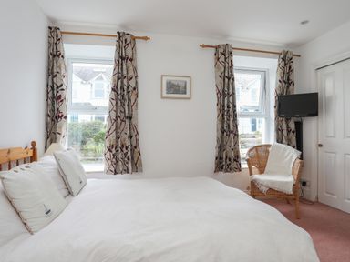 A bedroom with a double bed two windows with patterned curtains a wicker chair and a wall-mounted television at Alltwen in Borth-y-Gest