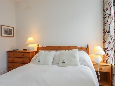 A bedroom with a wooden bed frame white bedding two white pillows with boat designs wooden nightstand with a lamp and wooden dresser with a lamp and a framed picture on the wall at Alltwen in Borth-y-Gest