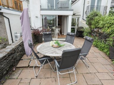 An outdoor patio with a round wooden table and six black chairs near sliding glass doors at Alltwen in Borth-y-Gest