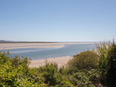 A sandy beach with water channel and greenery in the foreground at Alltwen in Borth-y-Gest