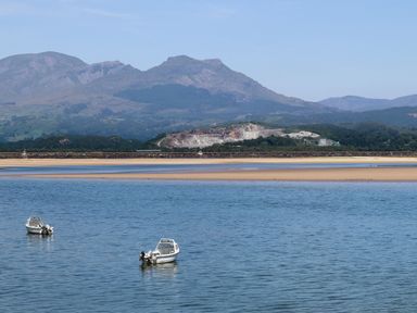 Two small boats floating on water with a sandy shore and mountains in the background at Alltwen in Borth-y-Gest