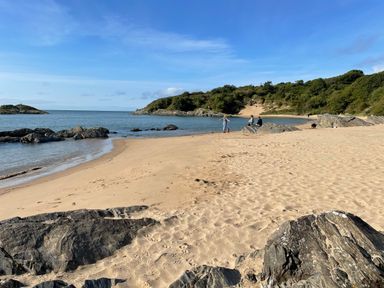 A sandy beach with rocks and people near the water at Alltwen in Borth-y-Gest