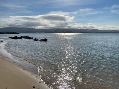 A sandy beach with water and rocks in the sea with mountains and clouds in the background at Alltwen in Borth-y-Gest