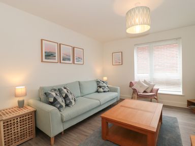 A living room with a sofa, armchair, coffee table, side table with lamp, and framed pictures on walls at Apartment 1 in Exmouth