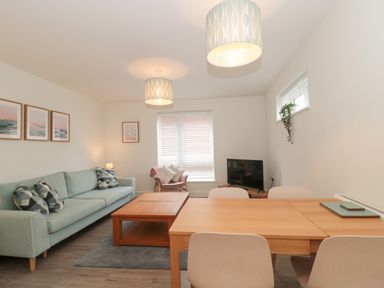 A living room with a sofa a coffee table a dining table chairs a TV and framed pictures at Apartment 1 in Exmouth