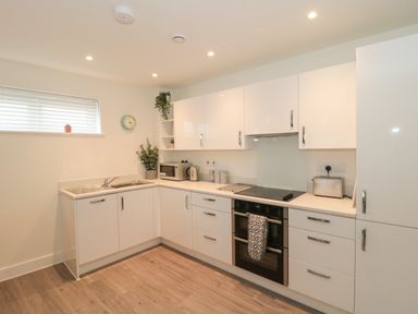 A kitchen with white cabinets microwave kettle oven and wooden floor at Apartment 1 in Exmouth