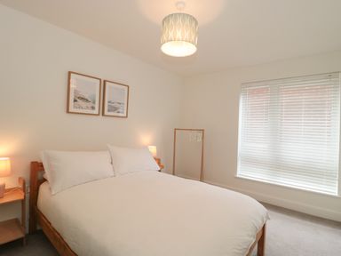 A bedroom with a double bed and white bedding two framed pictures on the wall bedside tables with lamps and a window with blinds at Apartment 1 in Exmouth