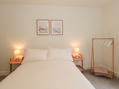 A bedroom with a bed two bedside tables with lamps a wooden clothes rack with hangers and folded blankets at Apartment 1 in Exmouth