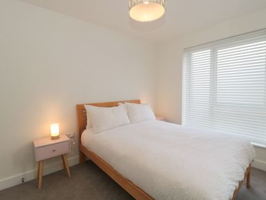 A bedroom with a wooden bed and white bedding next to a small bedside table with a lamp at Apartment 1 in Exmouth