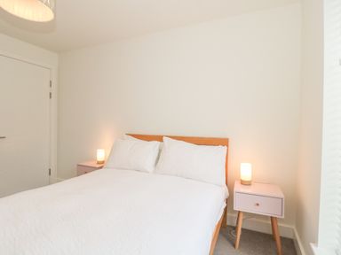 A bedroom with a bed with white bedding and two bedside tables with lamps at Apartment 1 in Exmouth