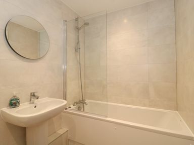 A bathroom with a sink a round mirror a bathtub and a shower at Apartment 1 in Exmouth