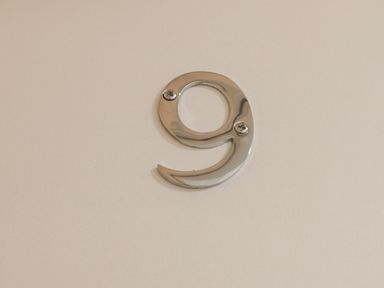 A metallic number 9 mounted on a plain white wall at Apartment 9 in Exmouth