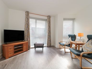 A living room with a television on a wooden stand and two armchairs with cushions at Apartment 9 in Exmouth
