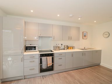 A kitchen with gray cabinets a microwave on the counter a toaster a kettle a sink and a clock on the wall at Apartment 9 in Exmouth