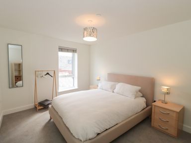 A bedroom with a double bed two bedside tables with lamps a clothes rack with hangers and a window at Apartment 9 in Exmouth