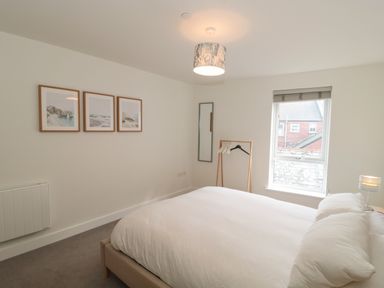 A bedroom with a bed a window three pictures on the wall and a clothes rack at Apartment 9 in Exmouth