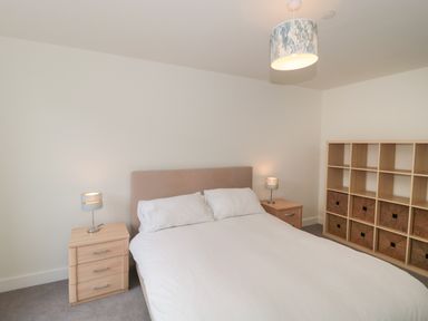 A bedroom with a double bed two bedside tables and a shelving unit with baskets at Apartment 9 in Exmouth