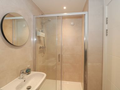 A bathroom with a white sink and faucet next to a glass-enclosed shower area with a showerhead and a round mirror on the wall at Apartment 9 in Exmouth