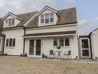 Outside view of a white two-story house with dormer windows and a small patio set with two chairs and a table with flowers at Bryn Eglwys Bach in Penmynydd near Llanfairpwllgwyngyll