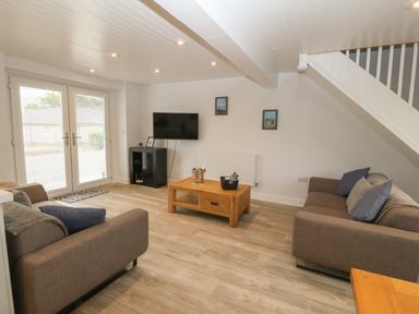 A living room with two sofas a wooden coffee table a TV on a stand and double glass doors at Bryn Eglwys Bach in Penmynydd near Llanfairpwllgwyngyll