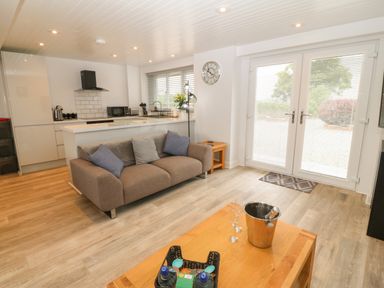 An open living area with a brown sofa, wooden coffee table, and a kitchen with white cabinets at Bryn Eglwys Bach in Penmynydd near Llanfairpwllgwyngyll