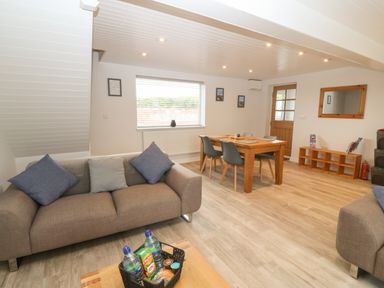 A living room with two sofas a dining table with chairs a window a door and a wooden shelf at Bryn Eglwys Bach in Penmynydd near Llanfairpwllgwyngyll