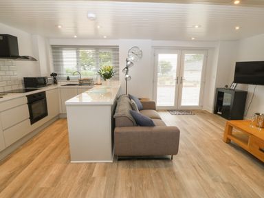 An open kitchen and living room with a sofa a wooden coffee table and a wall-mounted tv at Bryn Eglwys Bach in Penmynydd near Llanfairpwllgwyngyll