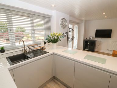 A kitchen with a black sink a drying rack flowers on a countertop and a wall clock at Bryn Eglwys Bach in Penmynydd near Llanfairpwllgwyngyll