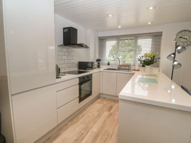 A kitchen with white cabinets a black oven and cooker a microwave a sink and a flower vase on a countertop at Bryn Eglwys Bach in Penmynydd near Llanfairpwllgwyngyll