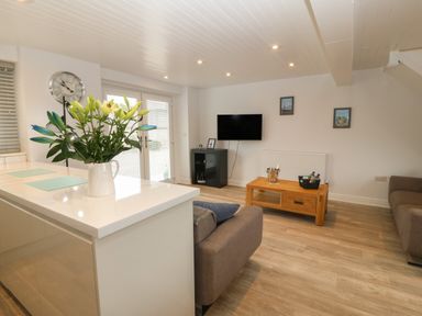 A living room with a wooden coffee table, a wall-mounted TV, a sofa, and flowers on a kitchen island at Bryn Eglwys Bach in Penmynydd near Llanfairpwllgwyngyll