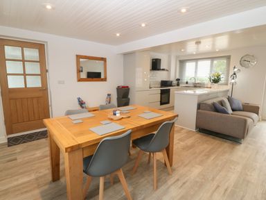 A dining area with a wooden table and chairs next to a kitchen and a sofa at Bryn Eglwys Bach in Penmynydd near Llanfairpwllgwyngyll