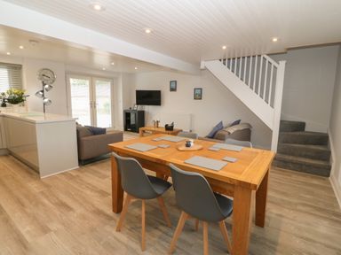 An open plan living and dining area with a wooden dining table and chairs a small seating area with sofas a wall-mounted tv and stairs at Bryn Eglwys Bach in Penmynydd near Llanfairpwllgwyngyll