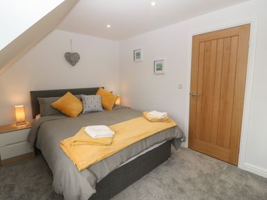 A bedroom with a double bed yellow and gray bedding bedside tables lamps wall decorations and a wooden door at Bryn Eglwys Bach Penmynydd near Llanfairpwllgwyngyll