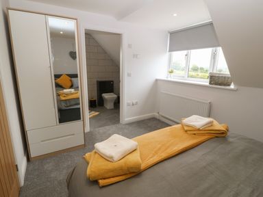 A bedroom with a bed, wardrobe with a mirror, window with blinds, and an ensuite bathroom at Bryn Eglwys Bach in Penmynydd near Llanfairpwllgwyngyll