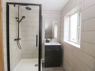 A bathroom with a shower enclosure and a sink with cabinet under a window at Bryn Eglwys Bach in Penmynydd near Llanfairpwllgwyngyll