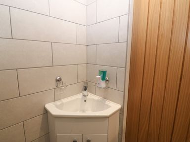A corner sink with soap dispenser and glass holder on tiled wall next to wooden door at Bryn Eglwys Bach in Penmynydd near Llanfairpwllgwyngyll