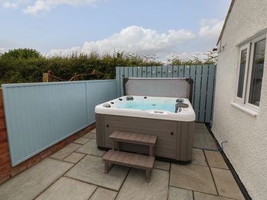 An outdoor hot tub with water and two steps on a stone patio next to a white building and blue wooden fences at Bryn Eglwys Bach in Penmynydd near Llanfairpwllgwyngyll