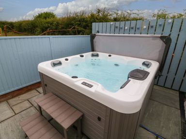An outdoor hot tub with steps on a stone patio surrounded by blue wooden fencing at Bryn Eglwys Bach in Penmynydd near Llanfairpwllgwyngyll