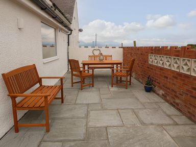 An outdoor patio with wooden bench and chairs around a table and a brick wall at Bryn Eglwys Bach in Penmynydd near Llanfairpwllgwyngyll