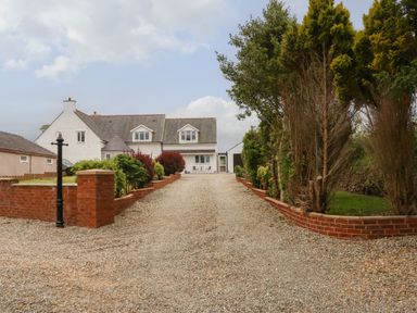Gravel driveway with brick retaining walls leading to a white two-story house with dormer windows at Bryn Eglwys Bach in Penmynydd near Llanfairpwllgwyngyll