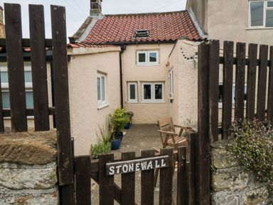 A small courtyard with potted plants and a wooden chair behind a wooden gate with a stone wall at Stonewall Sandsend