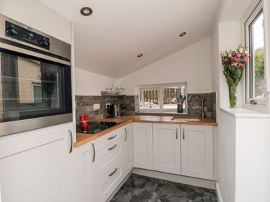 A kitchen with white cabinets wooden countertops a sink a stove an oven and flowers on a windowsill at Stonewall in Sandsend