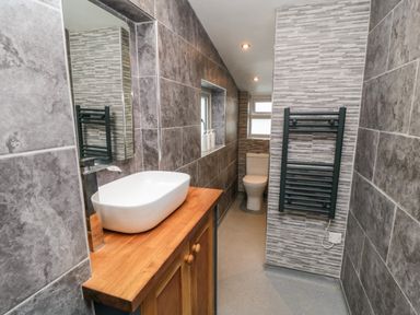 A bathroom with a wooden vanity and wash basin a mirror a toilet and a towel radiator at Stonewall in Sandsend