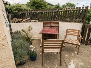 A small outdoor patio with wooden chairs a wooden table potted plants and logs stacked against a wall at Stonewall in Sandsend