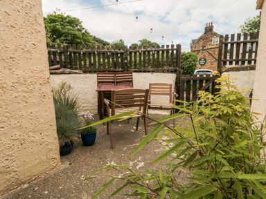 An outdoor patio area with wooden chairs a table potted plants and a wooden fence at Stonewall in Sandsend