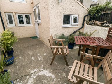 An outdoor patio area with wooden chairs wooden table potted plants and a door on a stucco exterior wall at Stonewall in Sandsend