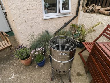 An outdoor patio with a metal barbeque grill wooden chairs potted plants and firewood stacked against a wall at Stonewall in Sandsend