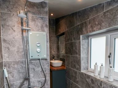 A shower area with a mounted shower unit next to a window with three labeled bottles in a bathroom at Stonewall in Sandsend